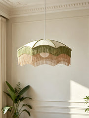 Close-up of a white fabric umbrella pendant light with layered green and pink fringe, illuminated.