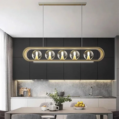 Modern gold linear pendant light with clear glass globes and an integrated LED light bar, mounted in a kitchen setting.