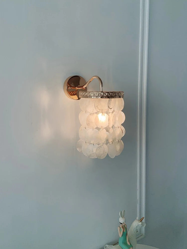 Gold wall sconce with cascading white shell accents mounted on a pale blue wall.
