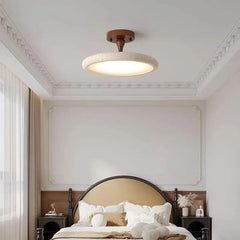 A bedroom scene featuring a dark wood and stone textured ceiling light fixture, with decorative elements on the wall and bed.