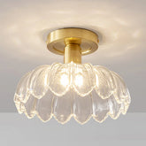 Close-up of a gold flush mount ceiling light with a clear glass shade shaped like flower petals, emitting a warm glow.