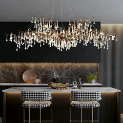 Modern kitchen with a long, cascading brass chandelier with clear teardrop crystals and black and white patterned bar stools.