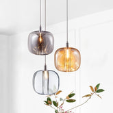 Three modern crystal ball pendant lights in clear, amber, and smoke gray hanging against a white wall.