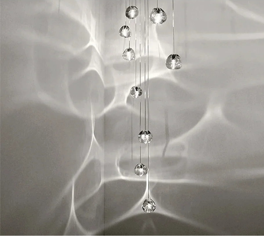 A long cascade of clear crystal ball pendant lights hanging against a textured wall, creating light reflections.