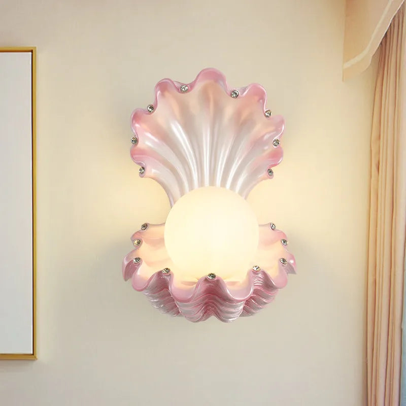 Pink seashell wall sconce with a frosted globe light and small crystal accents, mounted on a cream-colored wall.
