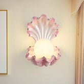 Pink seashell wall sconce with a frosted globe light and small crystal accents, mounted on a cream-colored wall.