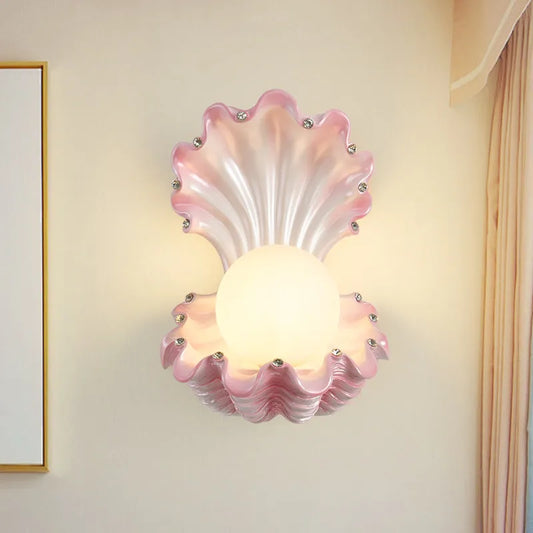 Pink seashell wall sconce with a frosted globe light and small crystal accents, mounted on a cream-colored wall.