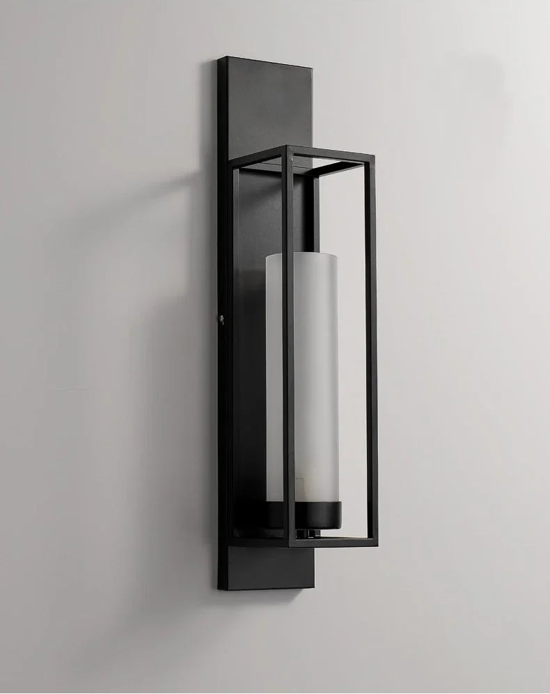 Modern wall-mounted light fixture with black frame and cylindrical glass shade on a gray background