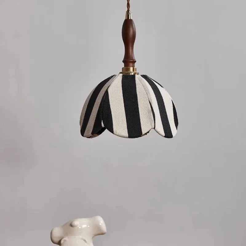 A black and white striped fabric pendant light hangs against a neutral background, showcasing its scalloped edge and wooden top.