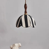 A black and white striped fabric pendant light hangs against a neutral background, showcasing its scalloped edge and wooden top.