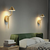Brass modern mushroom wall sconce mounted on a gray wall above a green headboard.