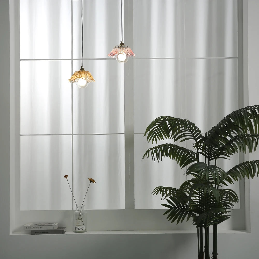 Two colorful glass pendant lights hanging in front of a large window with sheer curtains.