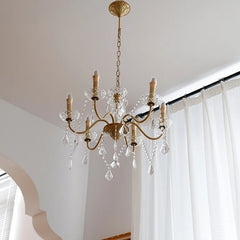 Gold chandelier with crystal accents hanging in a room with white curtains.