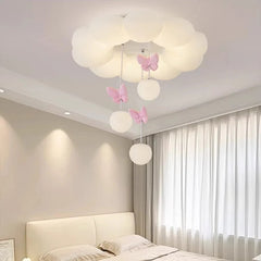 A white cloud-shaped ceiling light with pink butterflies and hanging orbs, illuminated in a room with curtains.