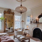 A large, ornate gold mirror reflects a Christmas tree and a living room setting, with a crystal orb chandelier hanging overhead.