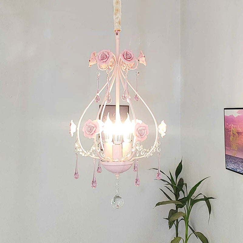 Pink floral crystal pendant light installed in a room with a plant and framed art on the wall.