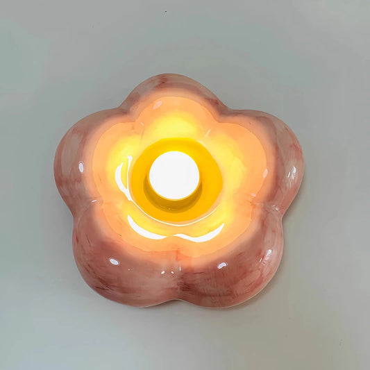 Pink ceramic petal wall sconce emitting warm light against a white wall.