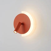 Orange modern LED wall lamp with a circular backplate and adjustable spotlight, emitting warm light against a white wall.