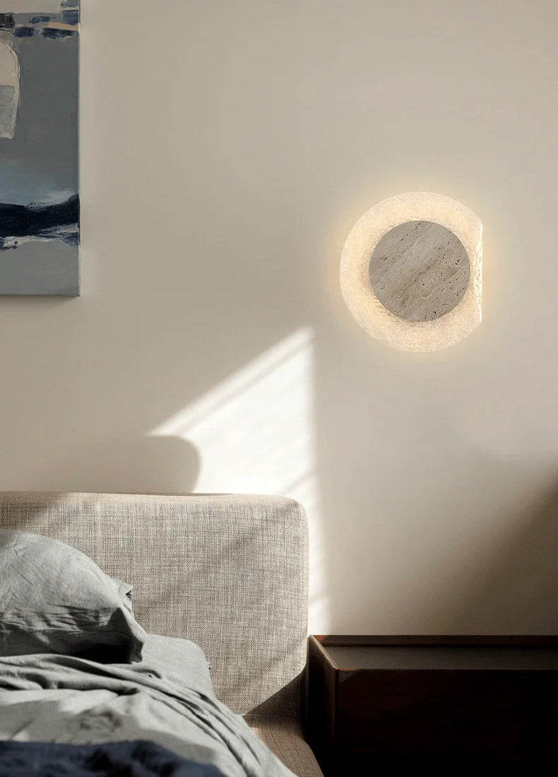 Round wall light fixture on a white wall above a bed with soft lighting.