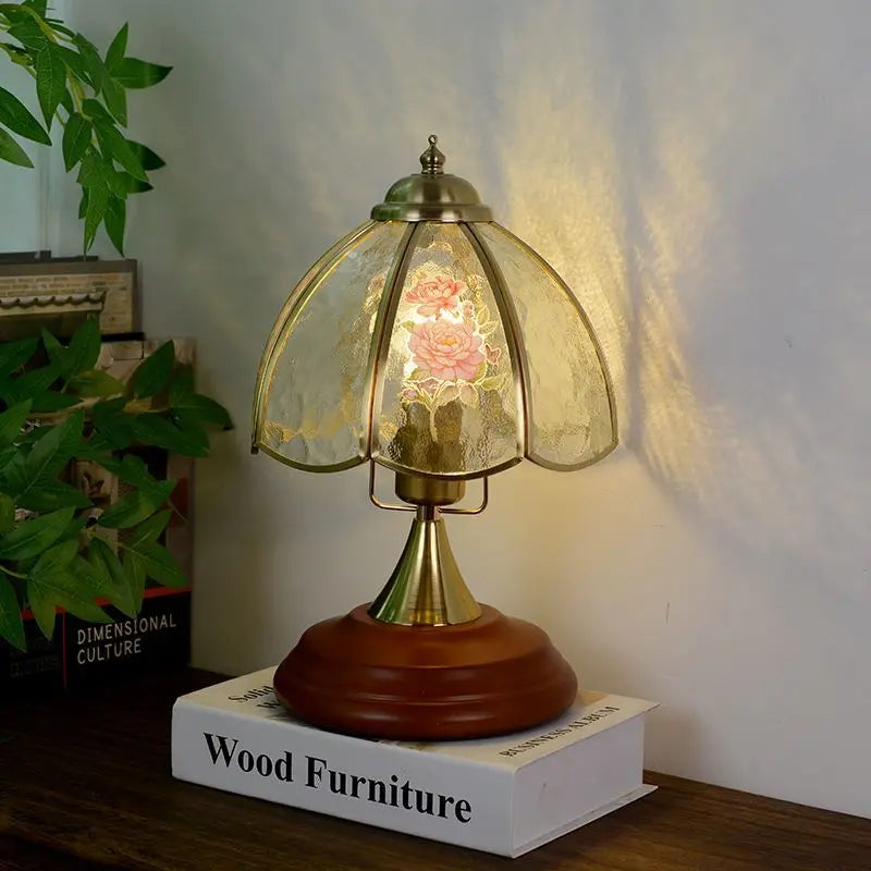 Brass table lamp with a bell-shaped glass shade featuring pink and white floral patterns, set on a wooden base.