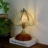 Brass table lamp with a bell-shaped glass shade featuring pink and white floral patterns, set on a wooden base.