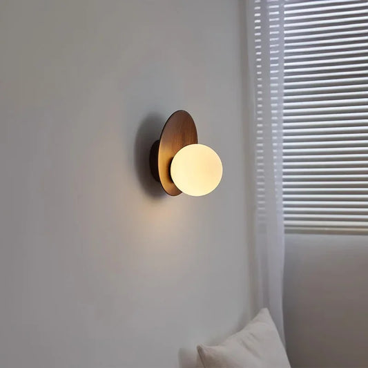 A modern wood arc wall sconce with a frosted glass globe, illuminated against a white wall.