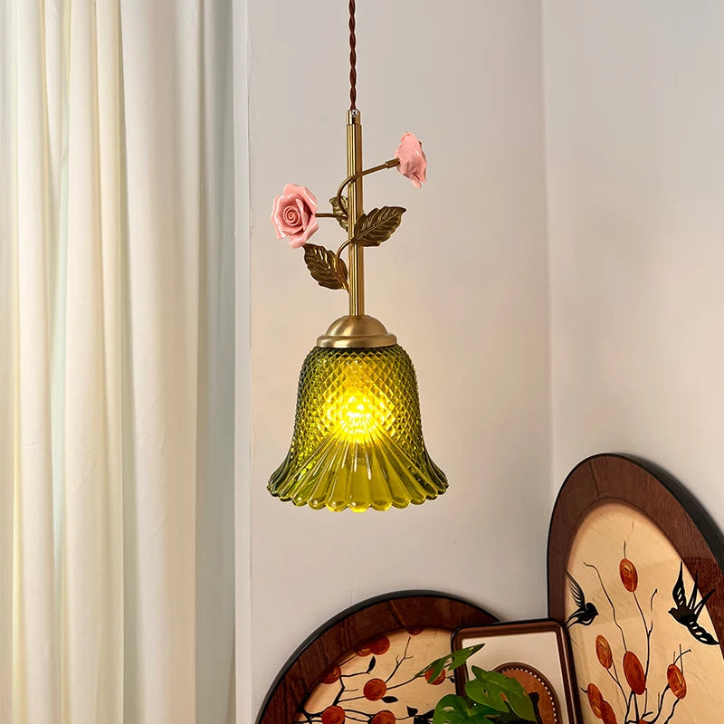 A pendant light with a green glass shade and a brass stem decorated with pink ceramic roses and leaves.