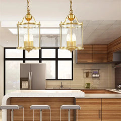 Two gold lantern pendant lights hanging above a kitchen island with wooden cabinetry and a modern refrigerator.