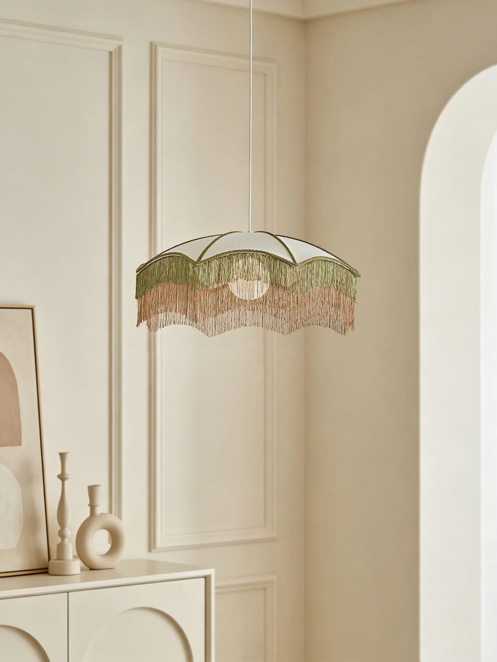 A white fabric umbrella pendant light with layered green and pink fringe hanging in a room with an arched doorway.