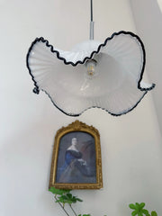 Floral-patterned lampshade with a light bulb inside, hanging above a framed portrait on a white wall.