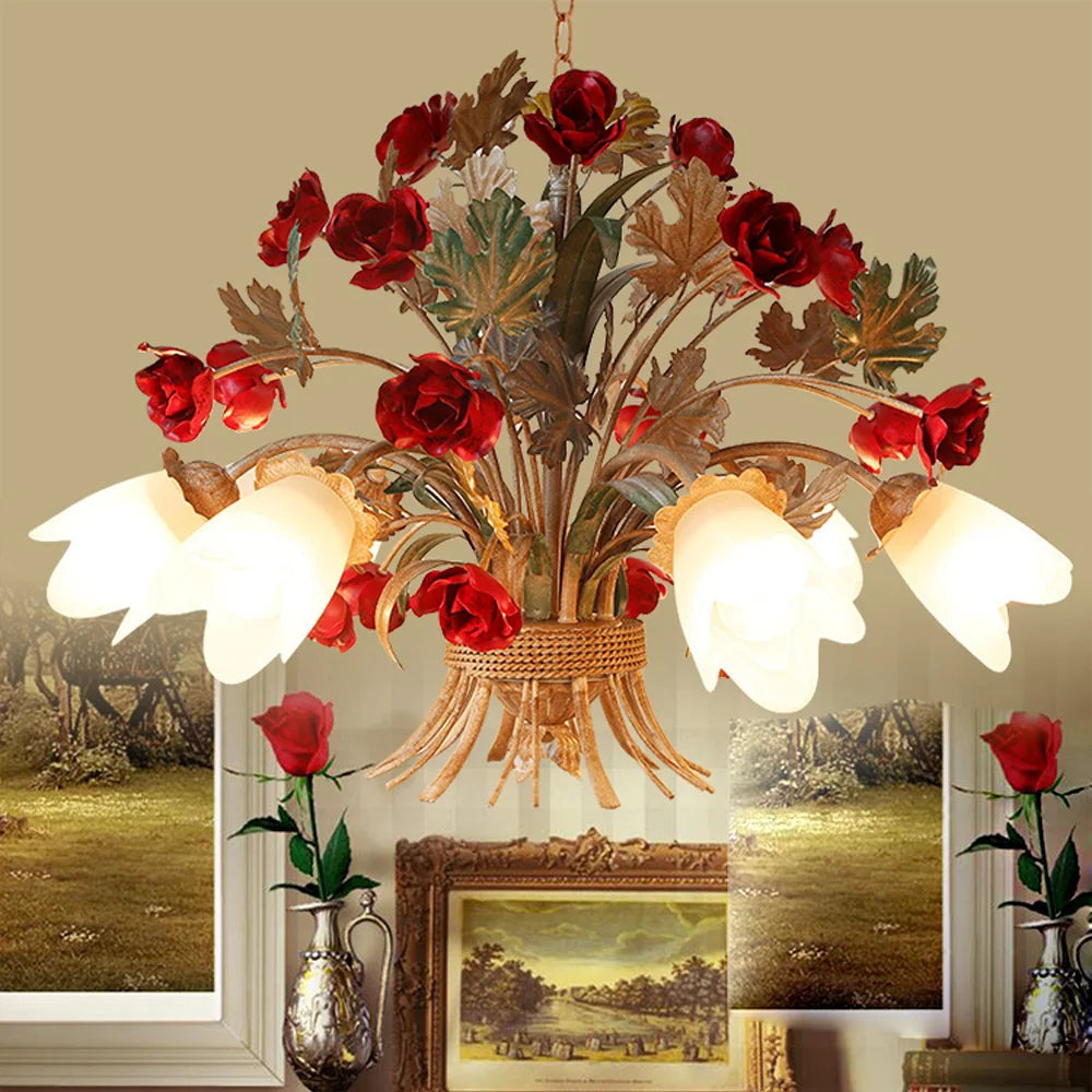A close-up view of a gold floral pendant light with red rose buds, green leaves, and frosted white tulip-shaped shades against a beige wall.