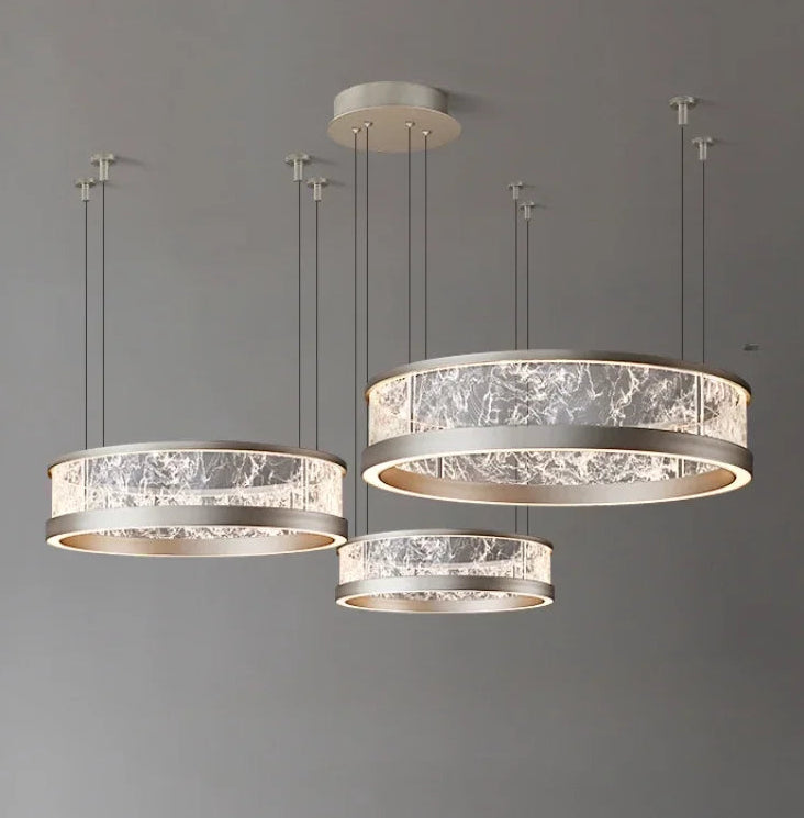 Collection of three ring-shaped pendant lights with textured glass diffusers and silver-toned metal frames, suspended from a grey ceiling.