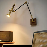 Brass and black adjustable swing arm wall sconce mounted on a white wall, with a walnut wood base.