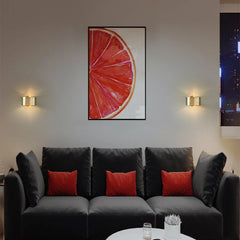 Modern living room with a gray sofa, red cushions, and a framed artwork of a pink grapefruit.
