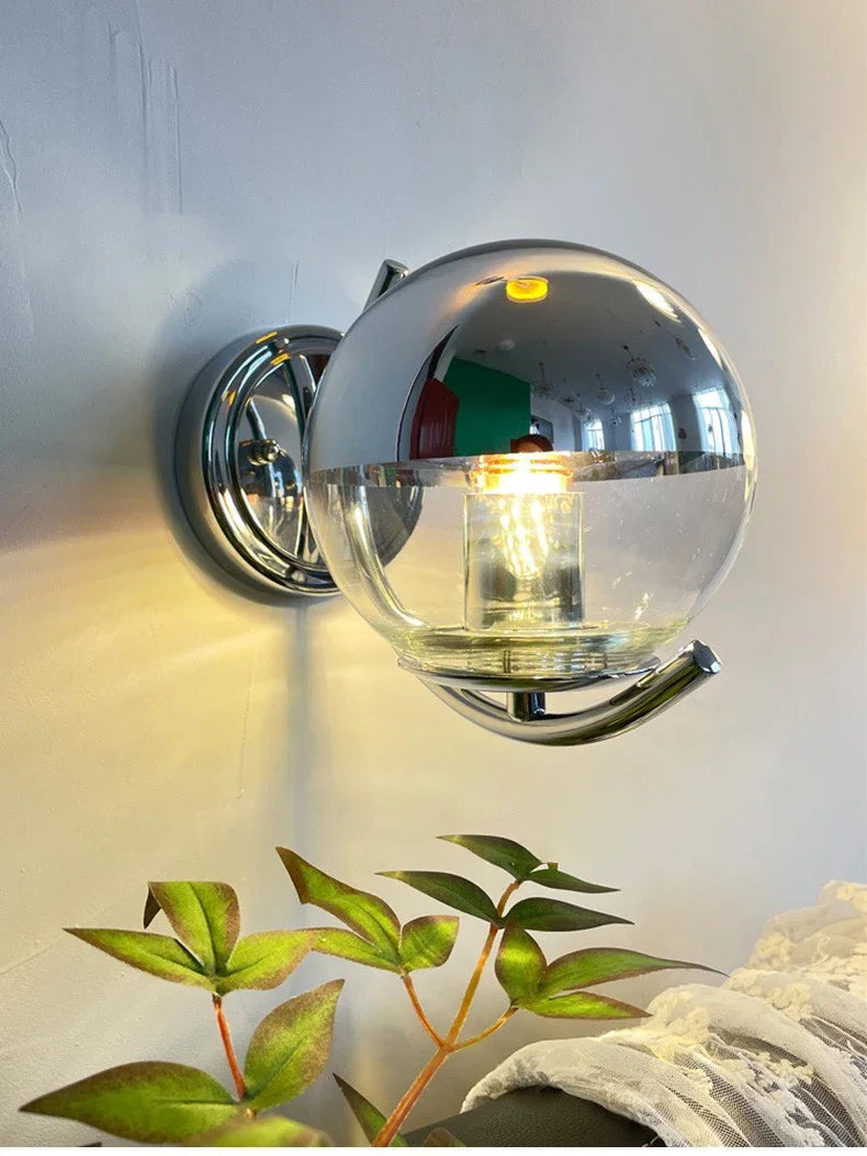 Wall-mounted light fixture with glass shade and metallic frame on a neutral wall.