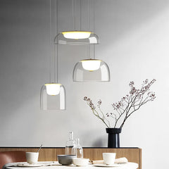 A dining table setting with three clear glass dome pendant lights with gold accents overhead.