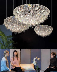 Two crystal chandeliers hanging above a modern living room with people sitting on a couch.