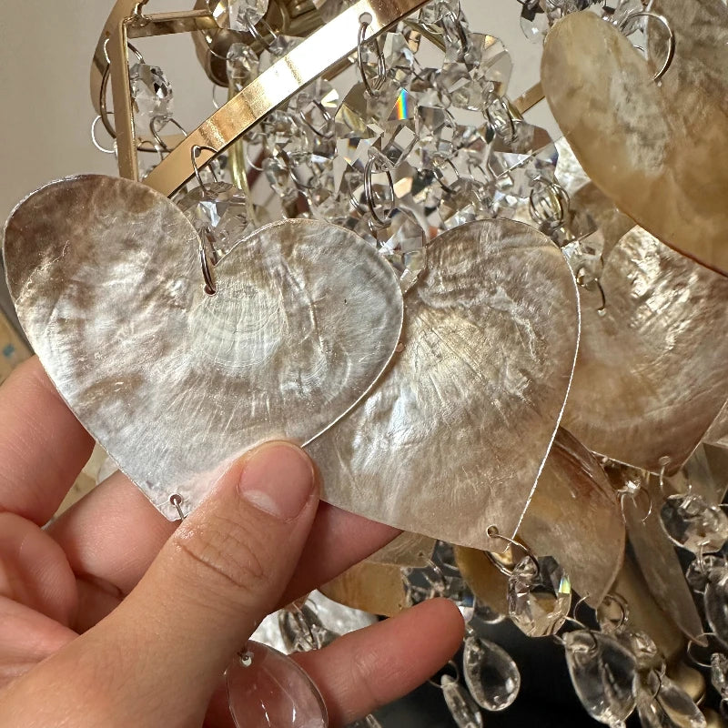 Close-up of a hand holding a pair of heart-shaped earrings with crystal accents.