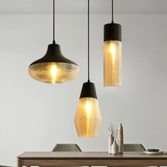 Three pendant lights with ribbed glass shades and dark tops hanging over a dining table.