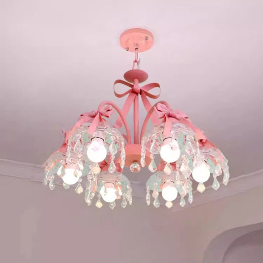 A pink chandelier with multiple arms adorned with pink bows and clear crystal droplets, hanging from a white ceiling.
