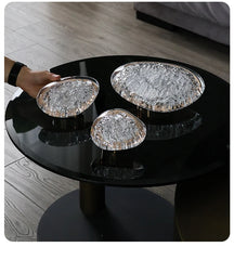Black round table with three decorative glass bowls on a wooden floor.
