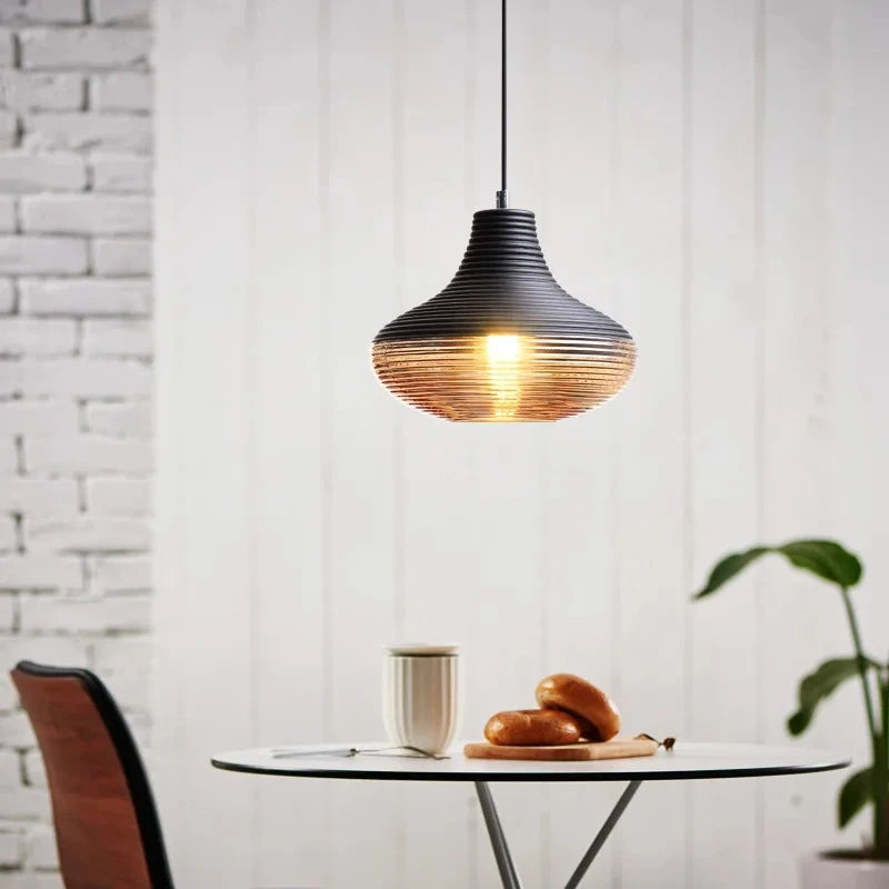 A single pendant light with a ribbed glass shade and dark top hanging above a small table.