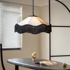 Fabric fringe pendant light with a white shade and black fringe, hanging above a dining table with blinds in the background.