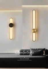 Modern wall lights on a white wall with a sofa and decorative items in the foreground.