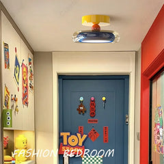 A colorful flush mount ceiling light with a yellow top, orange accent, and a blue and clear ring diffuser, installed in a brightly decorated room with a blue door.