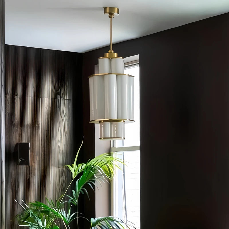 A gold and white acrylic tiered pendant light hanging in a dark wood paneled room near a window.