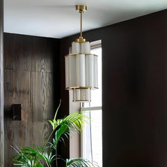 A gold and white acrylic tiered pendant light hanging in a dark wood paneled room near a window.