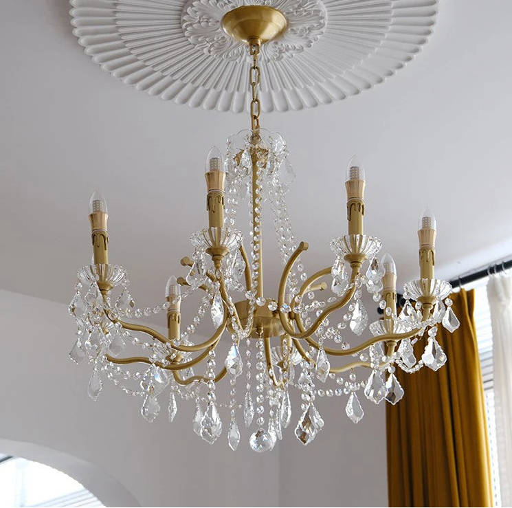 Gold chandelier with crystal accents hanging from a decorative ceiling.