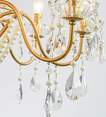 Gold chandelier with crystal and pearl accents on a light gray background