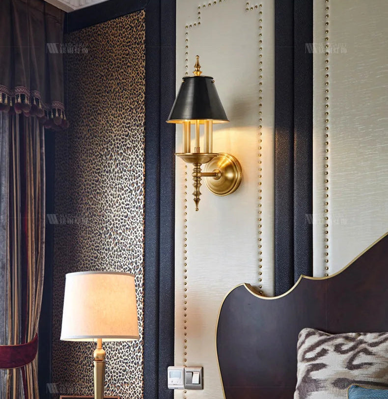 Decorative wall sconce and lamp in a bedroom setting with patterned wallpaper and headboard.